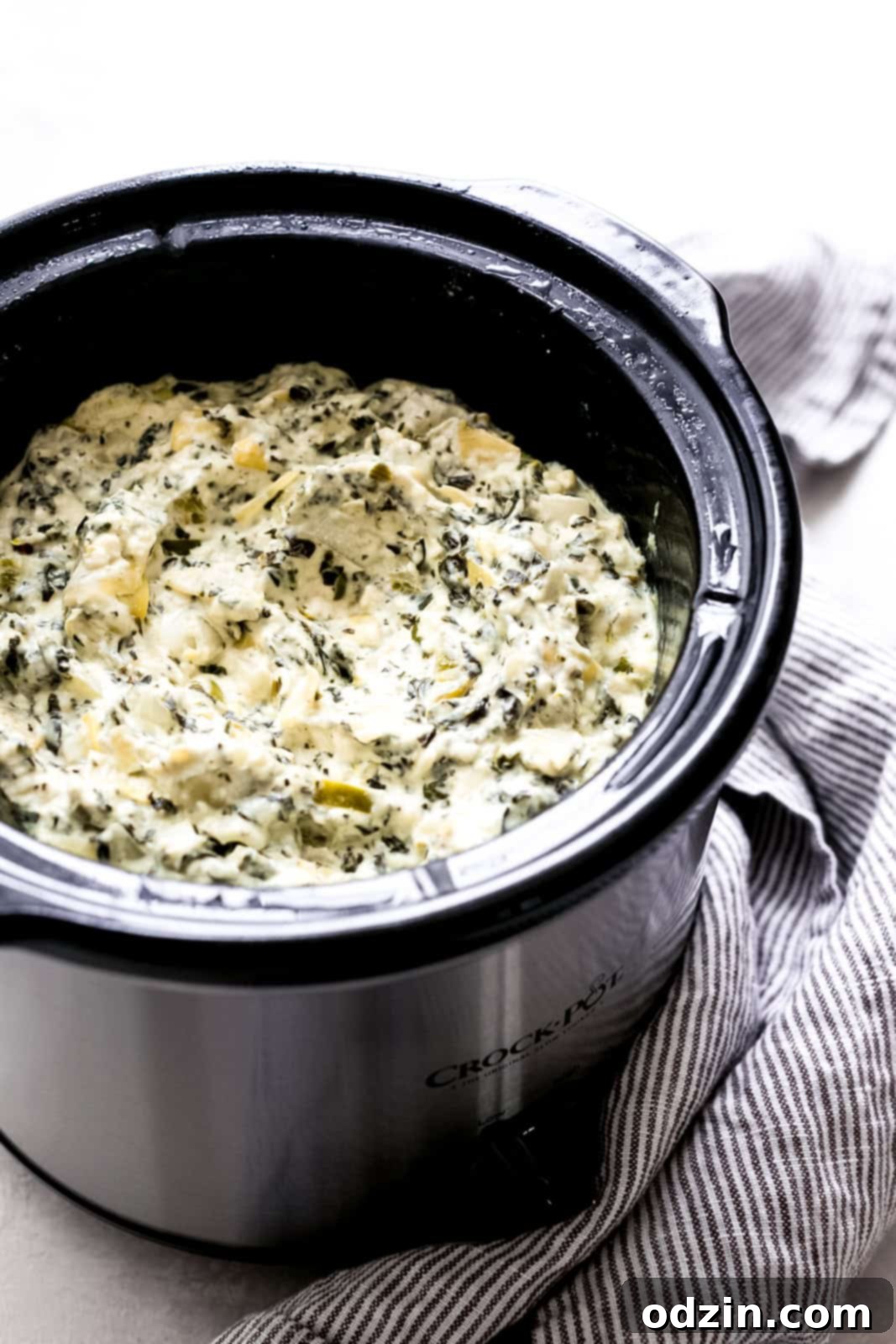 Effortless Slow Cooker Spinach Artichoke Dip 6 Slow cooker spinach artichoke dip prepared in slow cooker with a striped towel underneath