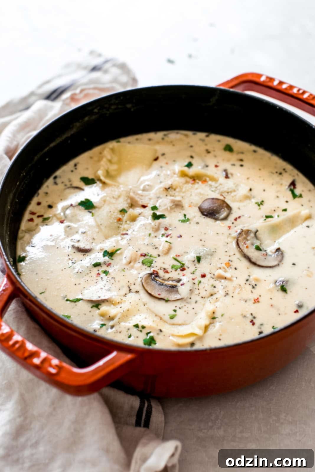 Large orange Dutch oven filled with prepared Roasted Garlic White Chicken Lasagna Soup on a grey surface