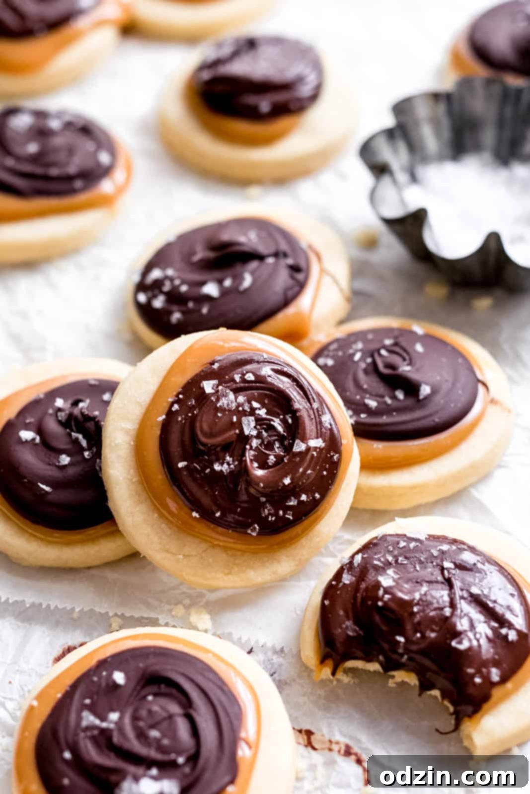 Copycat Twix Shortbread Cookies 9 scattered shortbread and chocolate cookies on parchment paper with bowl of flaked sea salt