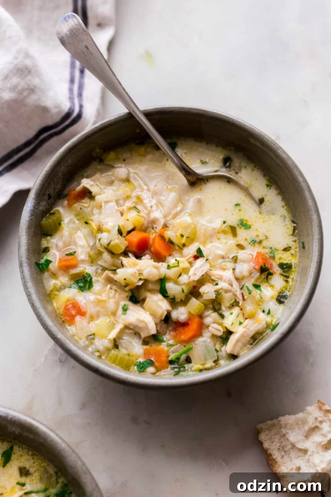 Sunshine Lemon Chicken Barley Soup 7 close up lemon chicken soup bowl with spoon resting on white marble