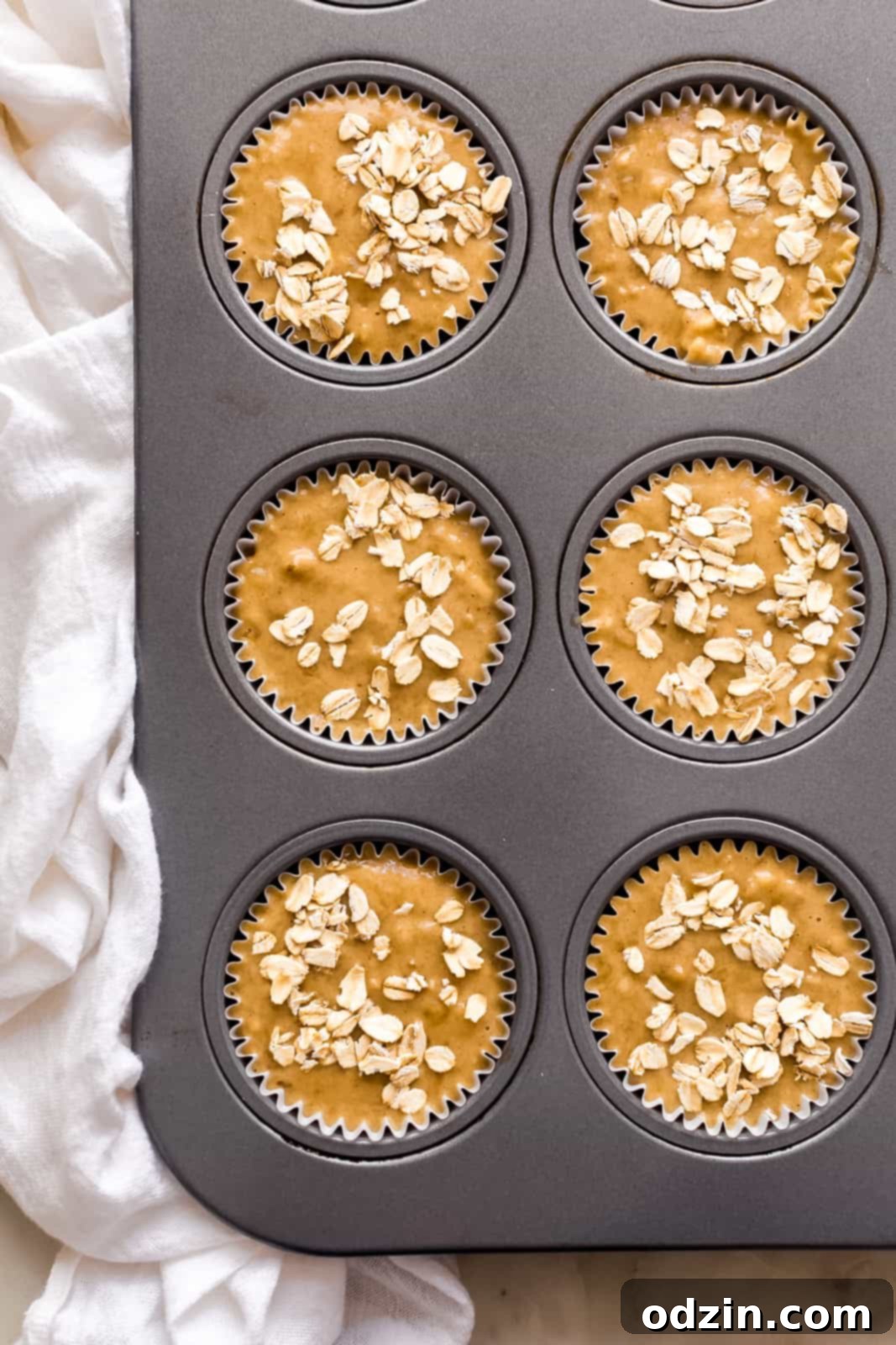 muffin pan lined with liners and filled with banana nut muffin batter topped with oats