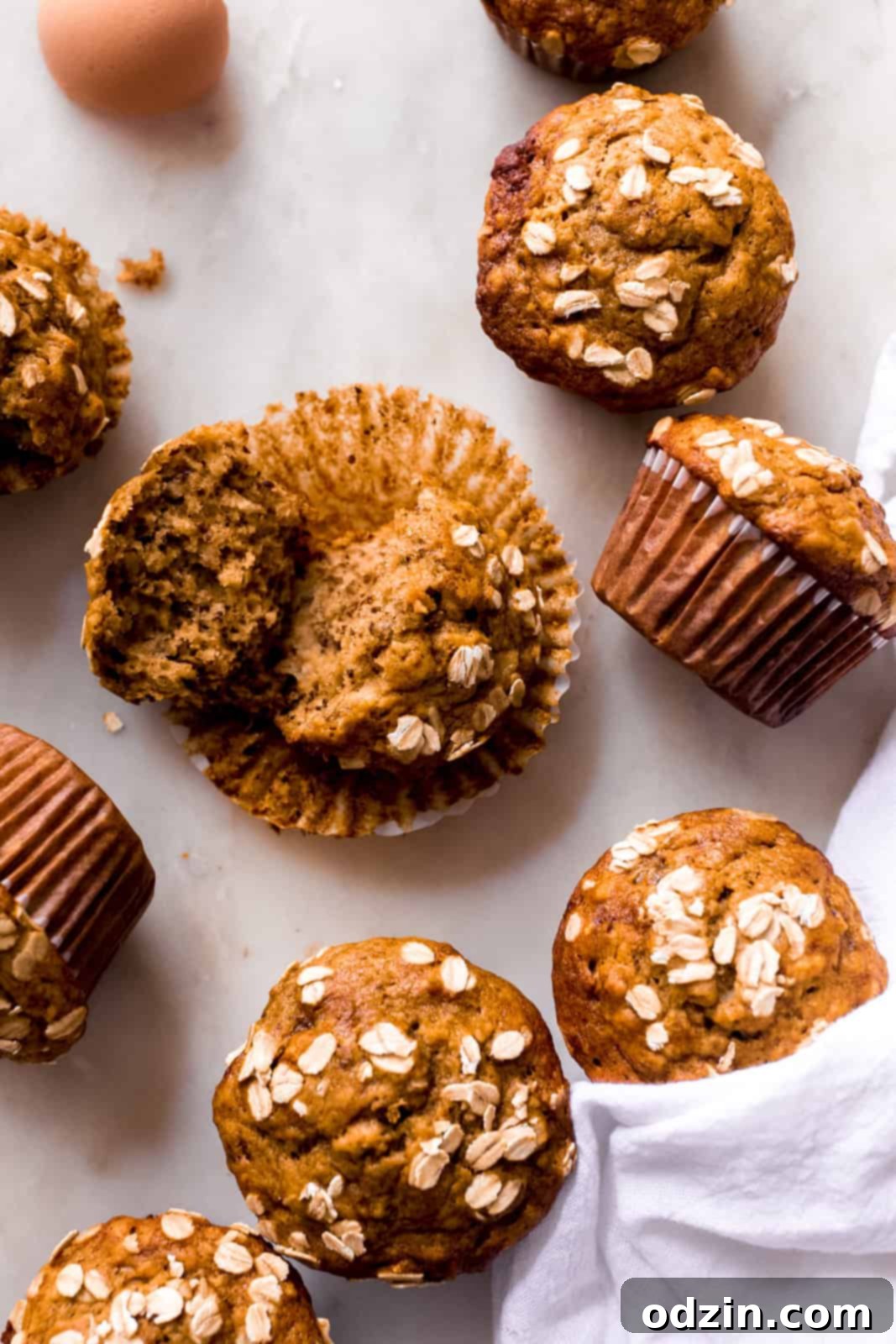 scattered banana nut muffins on white marble with one broken open to show texture