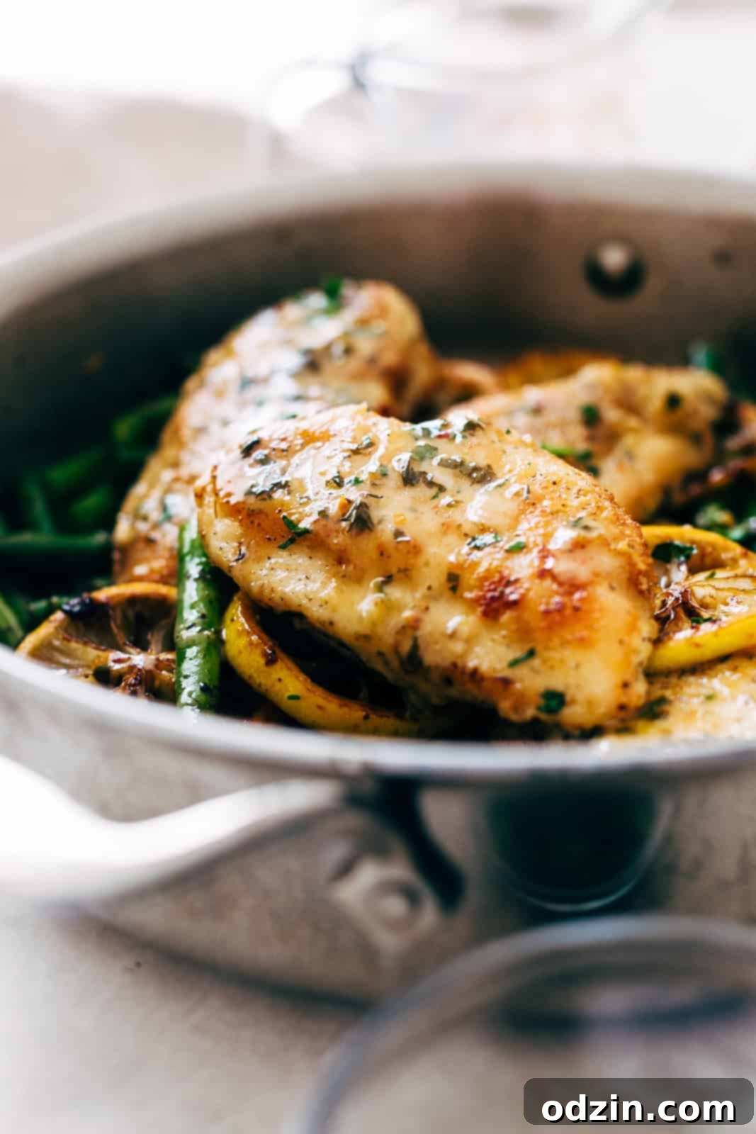 Close-up side view of a golden-brown pan-seared chicken breast generously drizzled with glossy lemon butter sauce, ready to be served