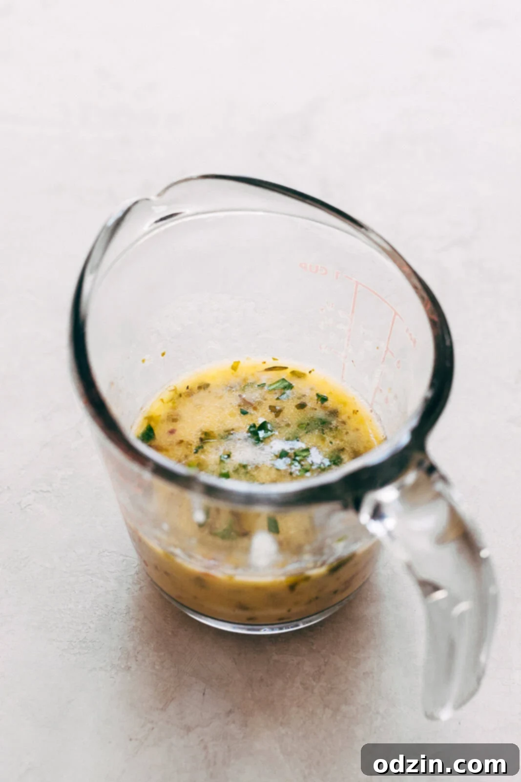 A measuring cup filled with a golden, aromatic lemon butter sauce, highlighting its smooth texture and rich color