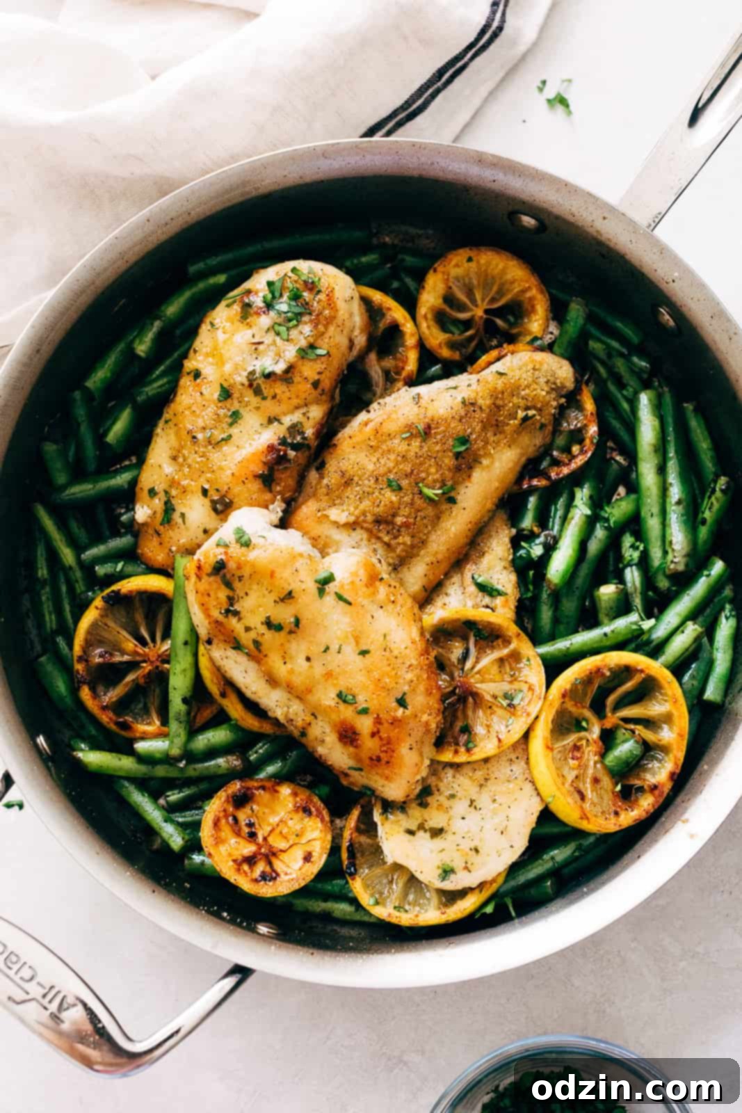 A cast iron skillet filled with beautifully seared chicken pieces, golden-brown lemon slices, and vibrant green beans, all cooking together