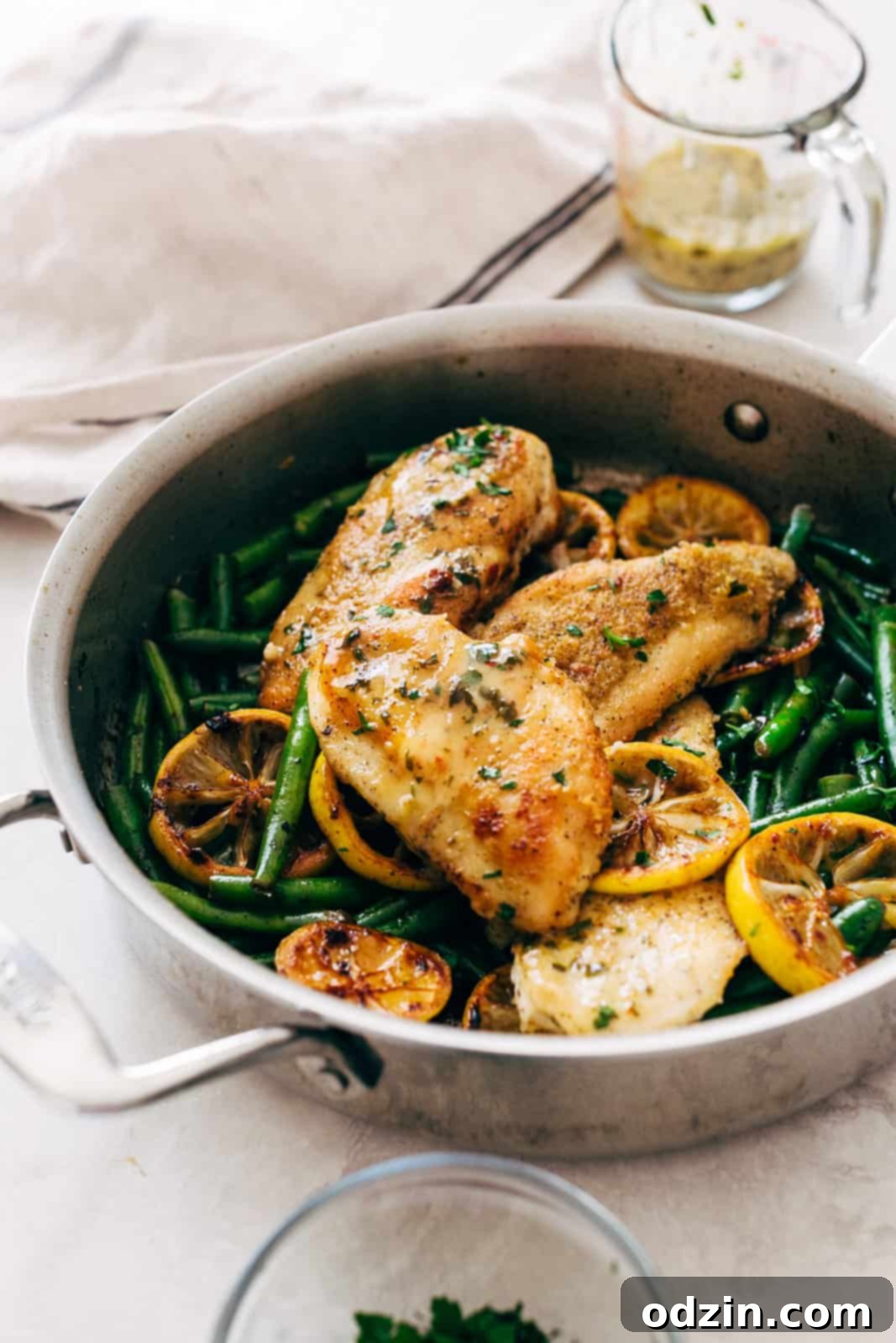 Skillet with cooked chicken breasts topped with fresh parsley and glistening with lemon butter sauce, ready to serve