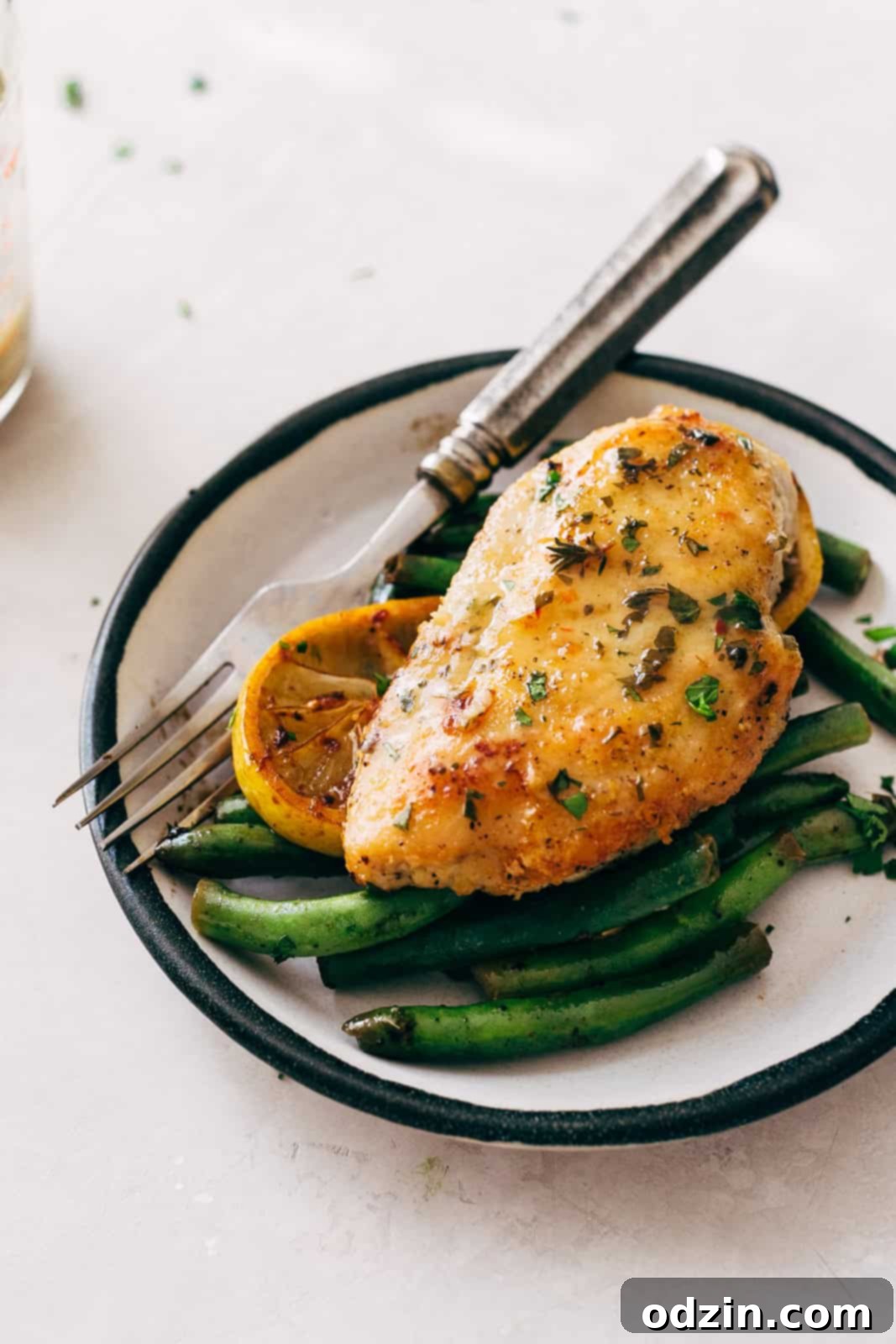 A black-rimmed plate holding a serving of sautéed green beans, perfectly cooked chicken breast, and a caramelized lemon slice, ready to be enjoyed