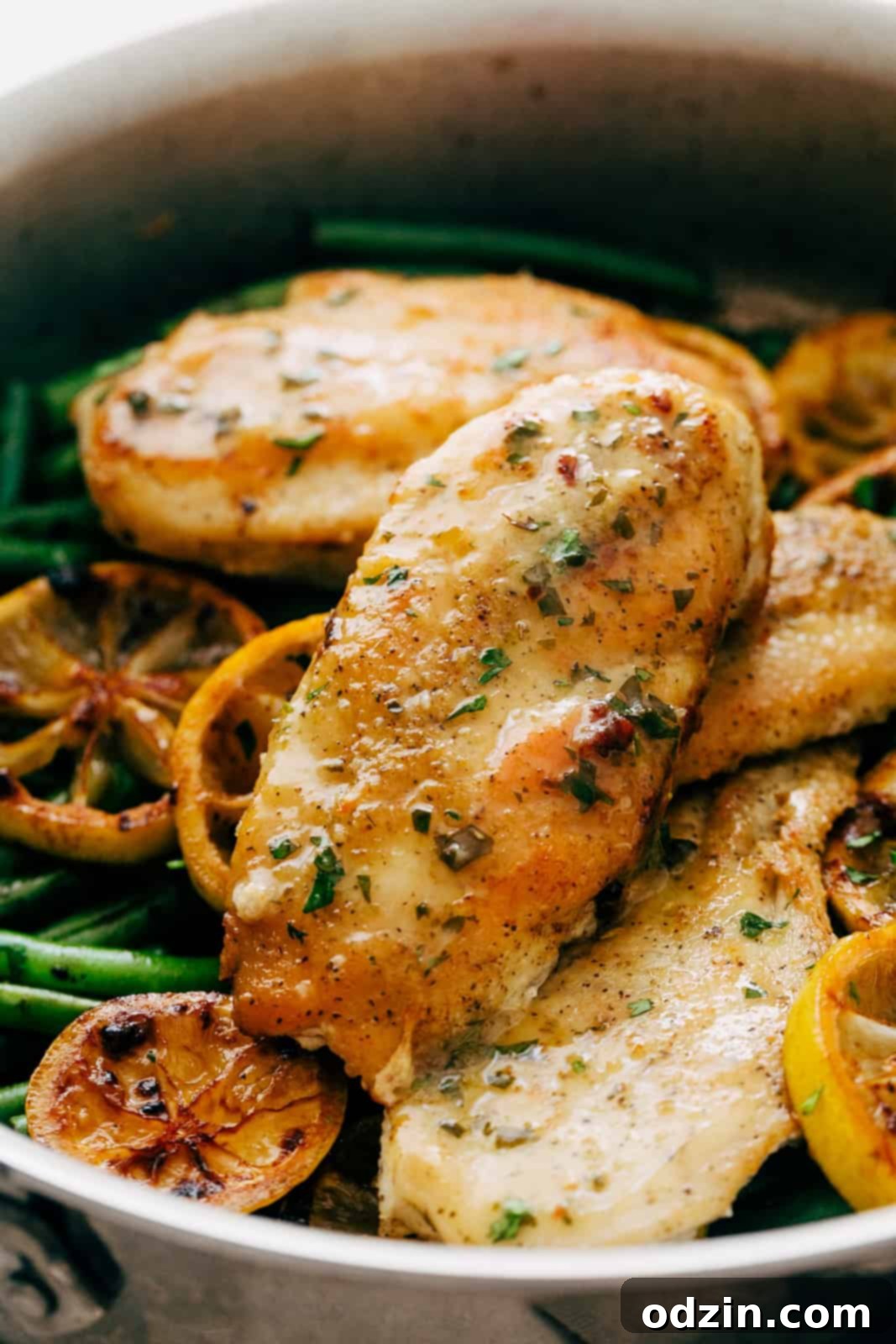Close-up shot of a perfectly cooked, golden-brown chicken breast in a skillet, glistening with a generous drizzle of lemon butter sauce
