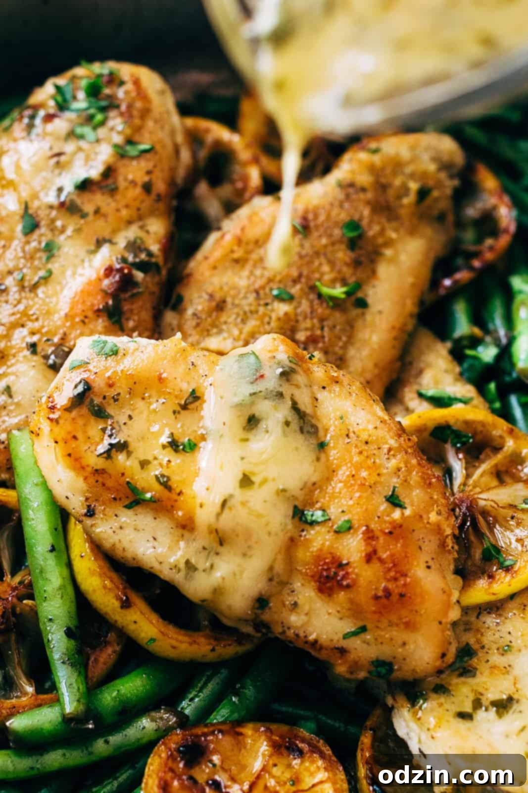 Visual of glossy lemon butter sauce being drizzled from a measuring cup over a browned chicken breast, showcasing its rich texture