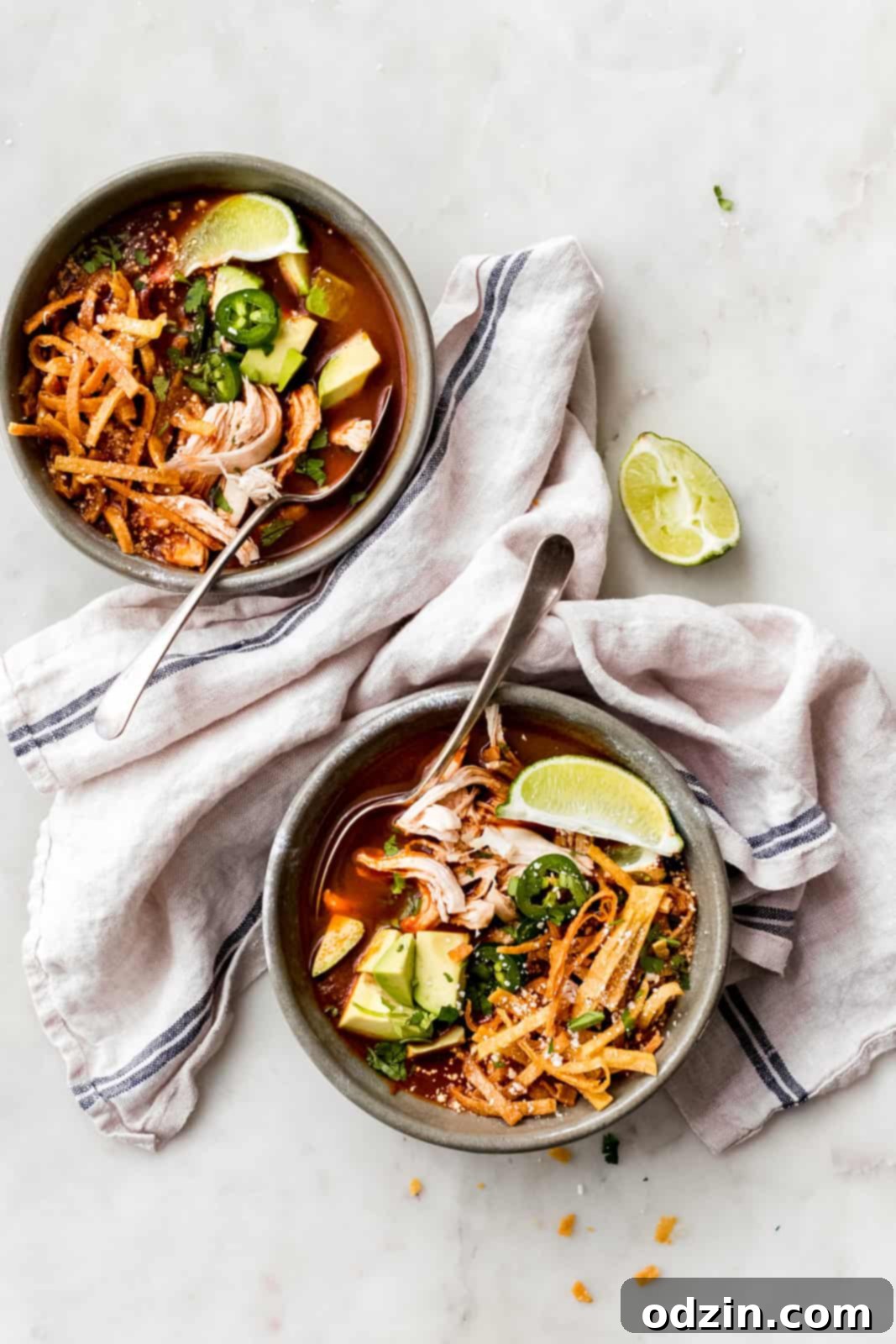 filled bowls with chicken tortilla soup, and crispy tortilla strips, jalapeno slices, lime wedges, and diced avocados