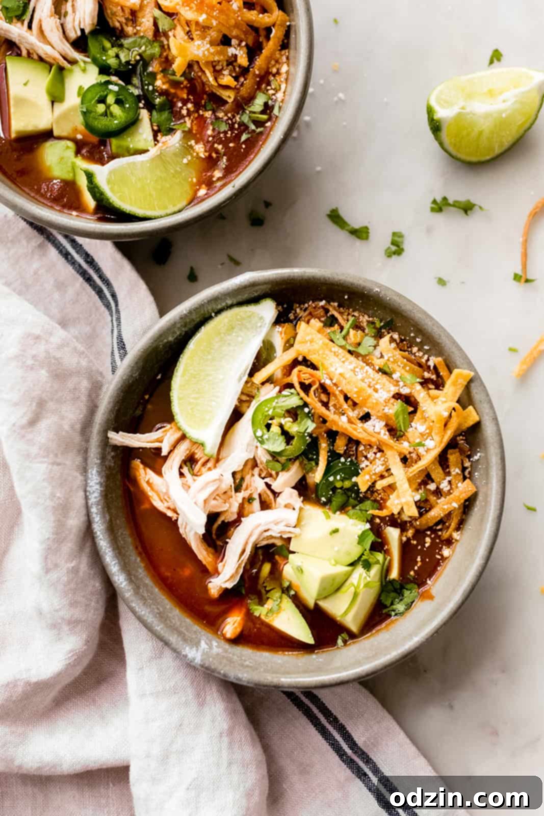 bowls of soup topped with fresh lime wedges, jalapeños, diced avocados, tortilla strips