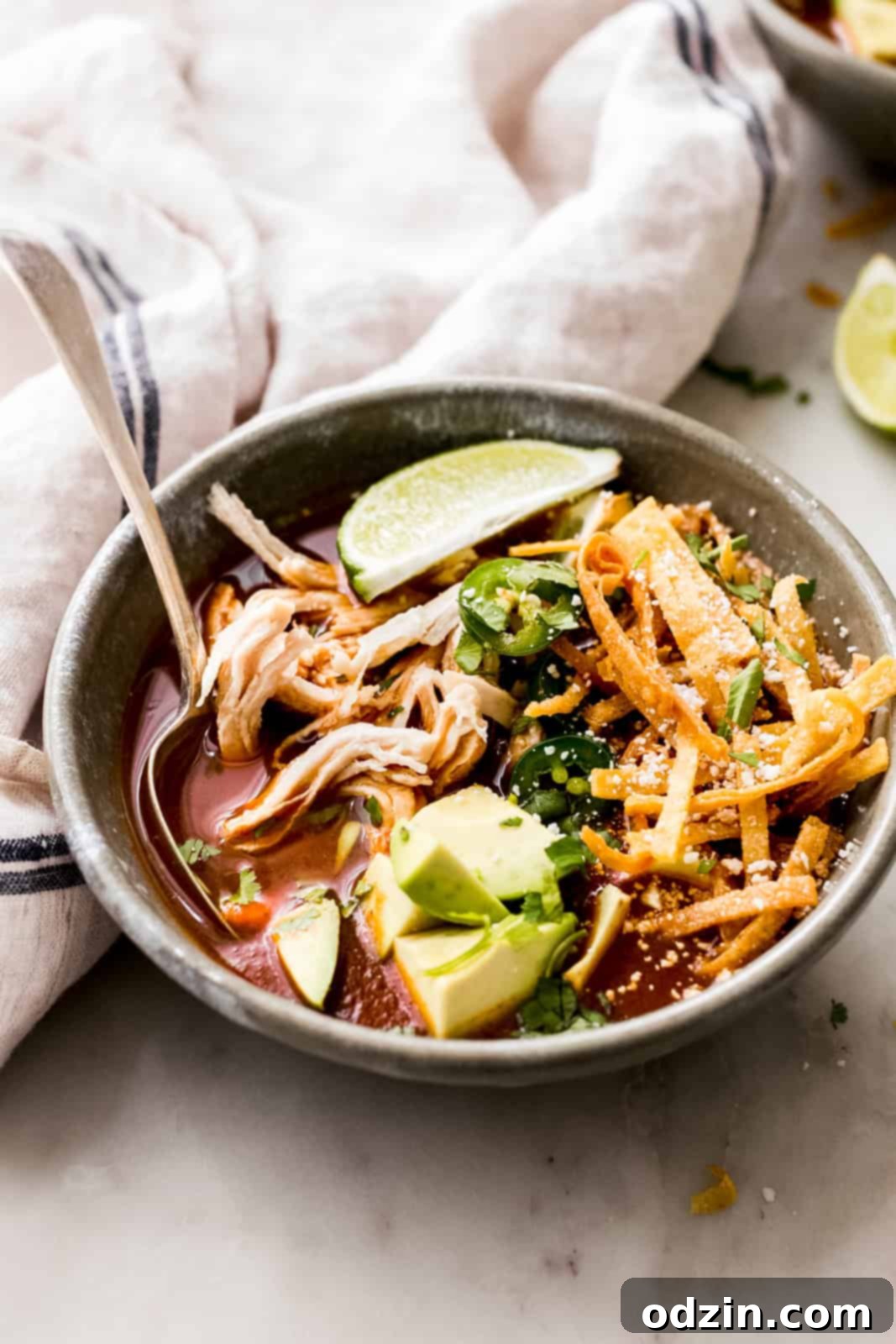 side shot of chicken tortilla soup bowl loaded with diced avocado, lime wedges, and crispy tortillas