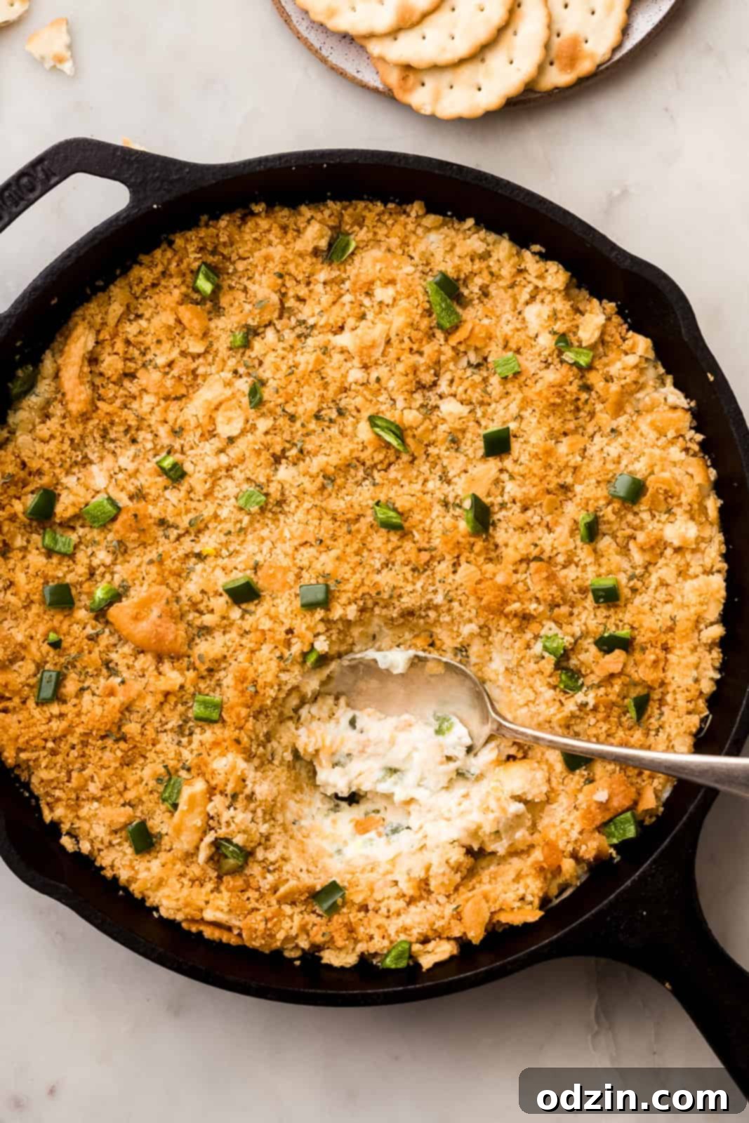 Spoon lifting a scoop of bubbly, warm jalapeño popper dip from a cast iron skillet