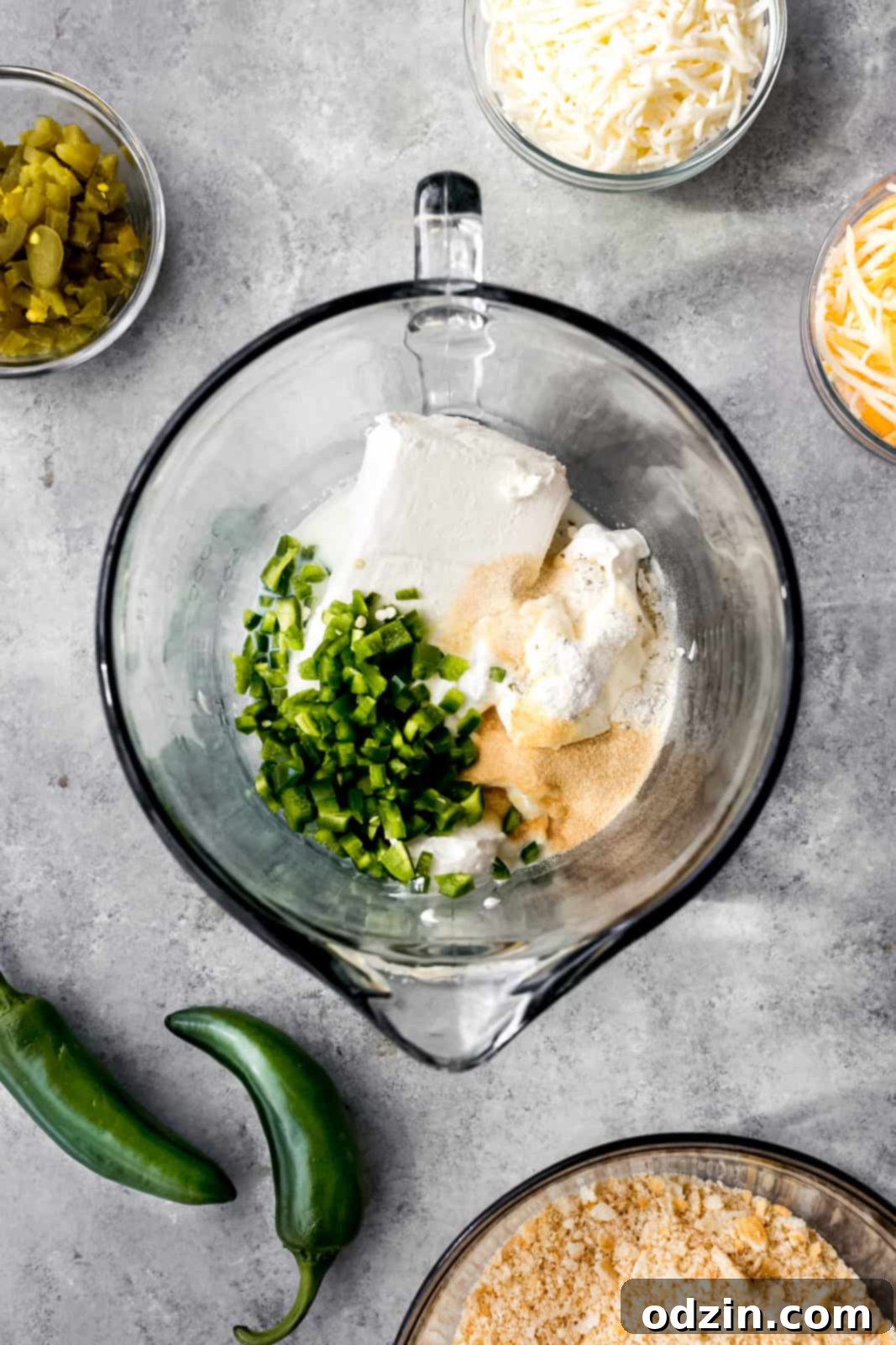Various fresh ingredients for jalapeño popper dip laid out on a gray surface, including cream cheese, jalapeños, and shredded cheese