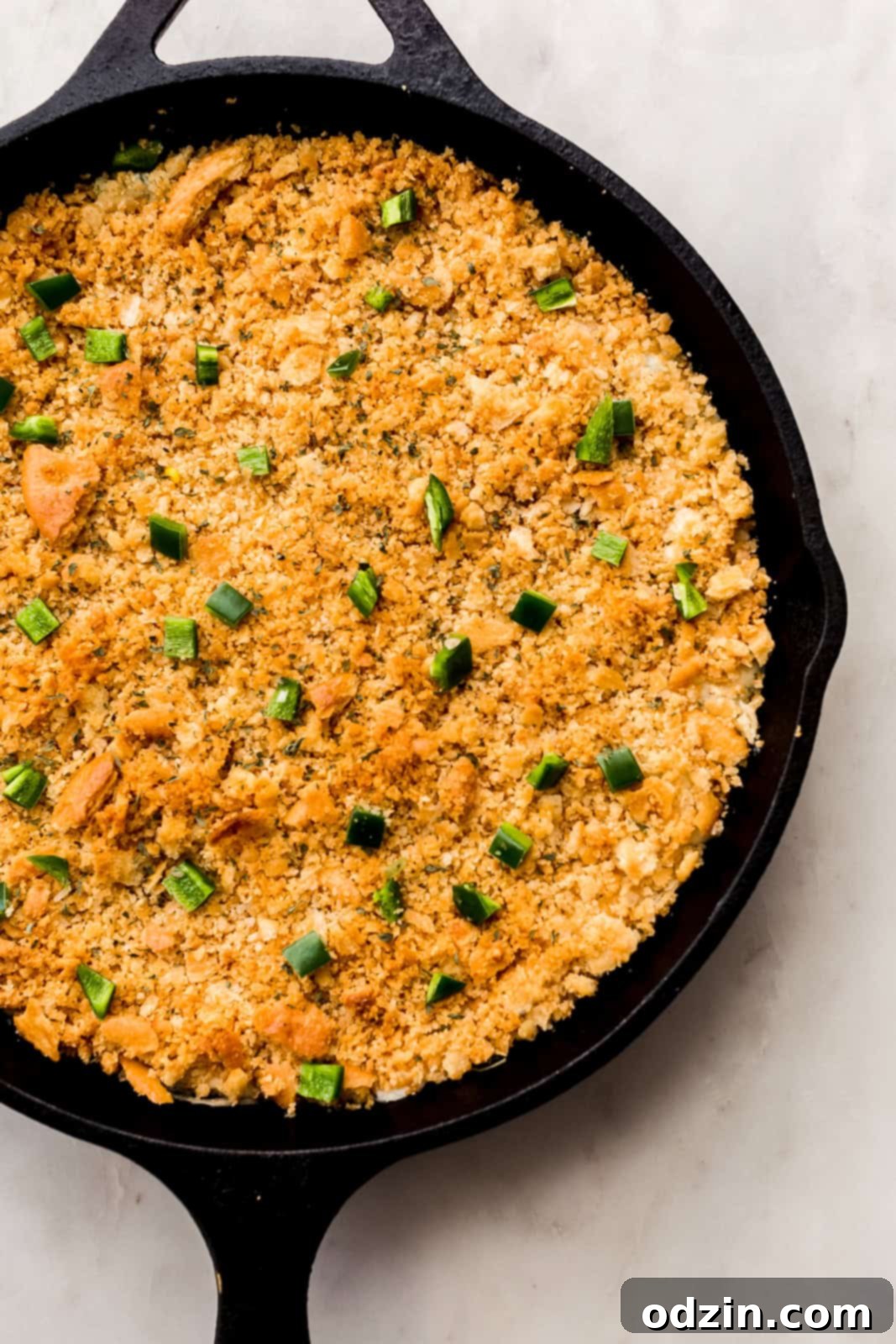 Undisturbed, golden-brown jalapeño popper dip topped with cracker crumbs, fresh out of the oven in a cast iron skillet