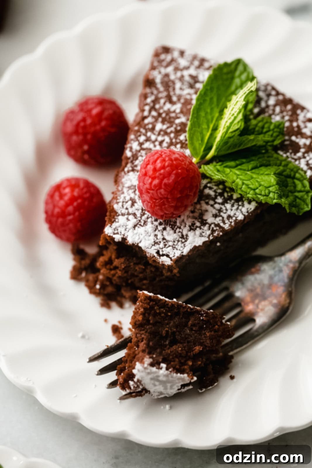 Caprese Flourless Chocolate Cake 3 slice of flourless chocolate cake with raspberries, powdered sugar, and mint with a broken piece on a fork