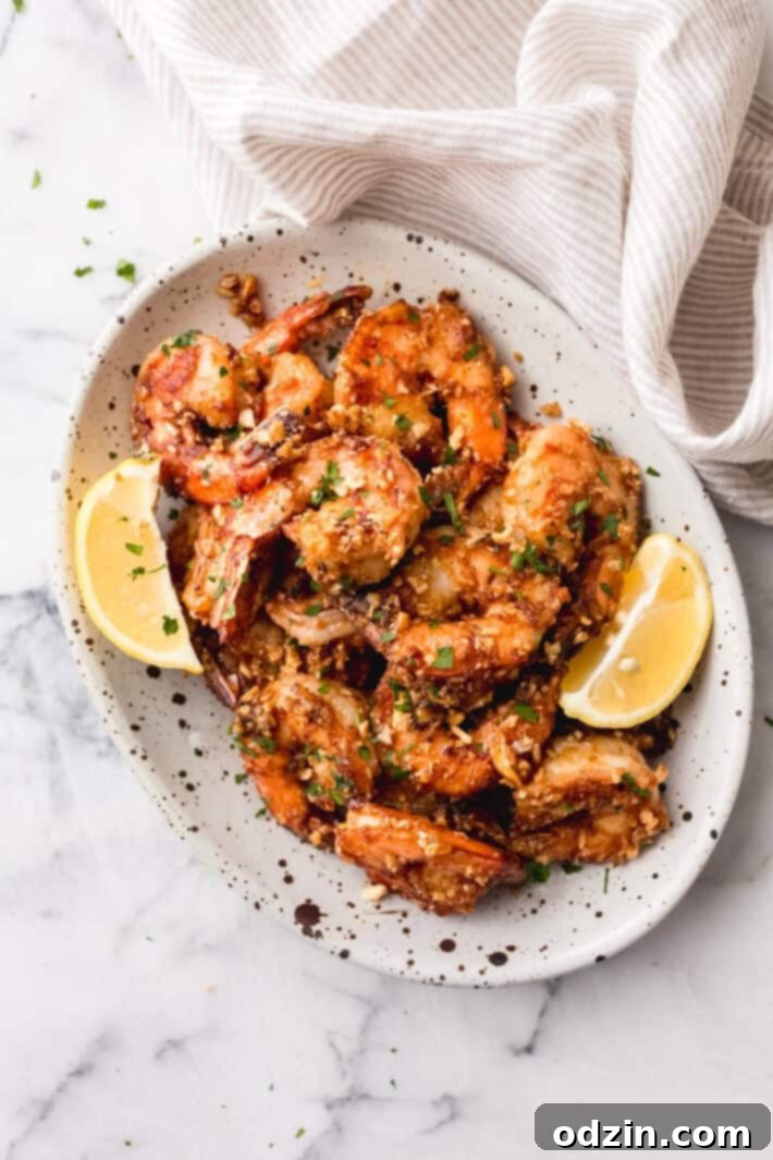 Hawaiian garlic shrimp with lemon wedges on speckled plate on marble surface, garnished with fresh herbs