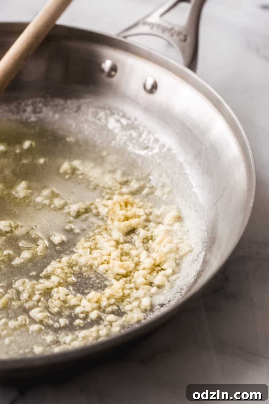 Sautéing fresh minced garlic in a stainless steel pan with butter and oil