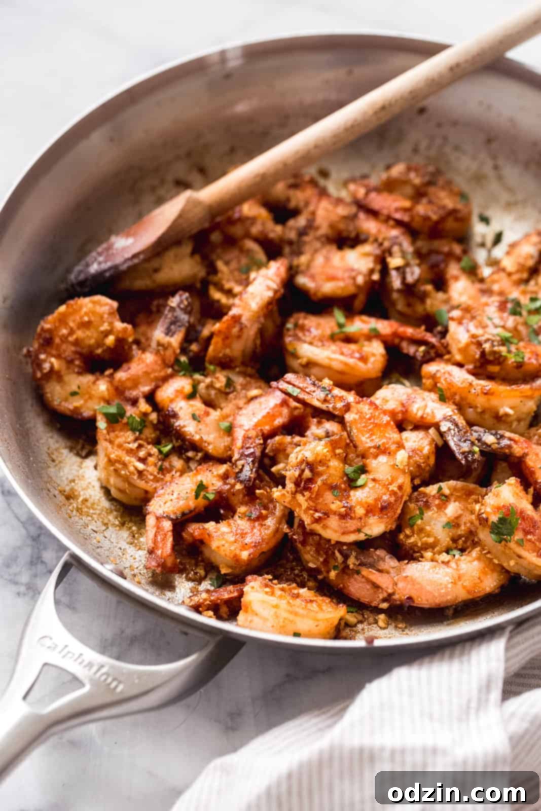 Skillet with prepared Hawaiian shrimp scampi, a wooden spoon resting in the pan, ready for serving
