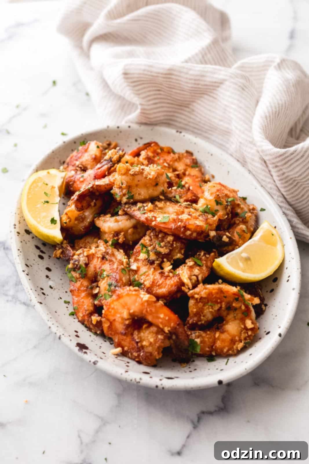 Prepared garlic shrimp on a white speckled plate on a white marble surface, garnished with fresh herbs