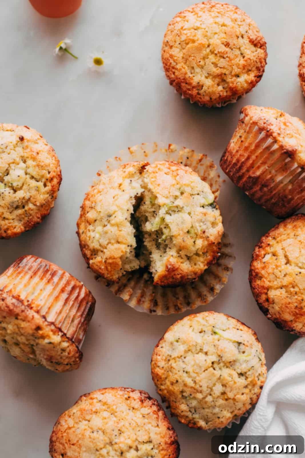 Freshly Baked Lemon Zucchini Muffins 2 scattered lemon zucchini muffins on white marble with tiny flowers