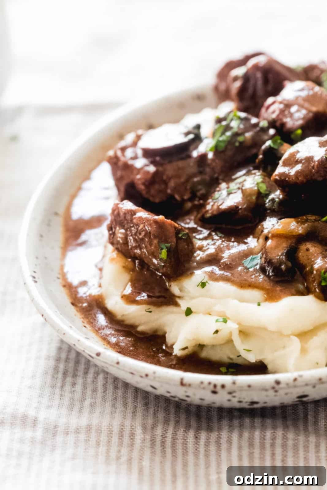 Tender Beef Tips with Savory Mushroom Gravy Slow Cooker Instant Pot 8 striped surface with speckled bowl with mashed potatoes topped with prepared tips sprinkled with parsley