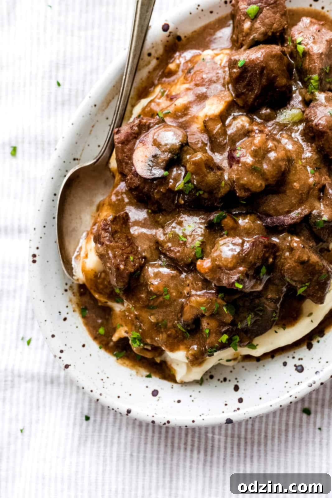 Tender Beef Tips with Savory Mushroom Gravy Slow Cooker Instant Pot 9 speckled bowl with a spoon resting with mashed potatoes topped with mushroom gravy and beef tips