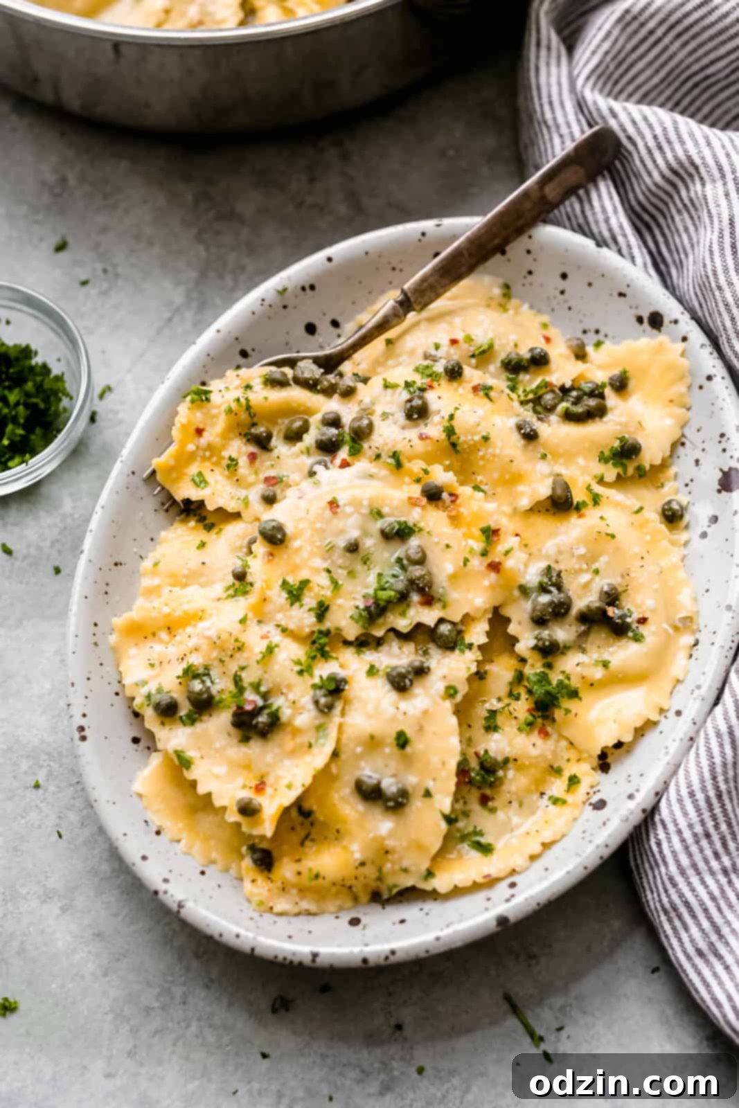 speckled oval serving dish with ravioli piccata topped with additional capers