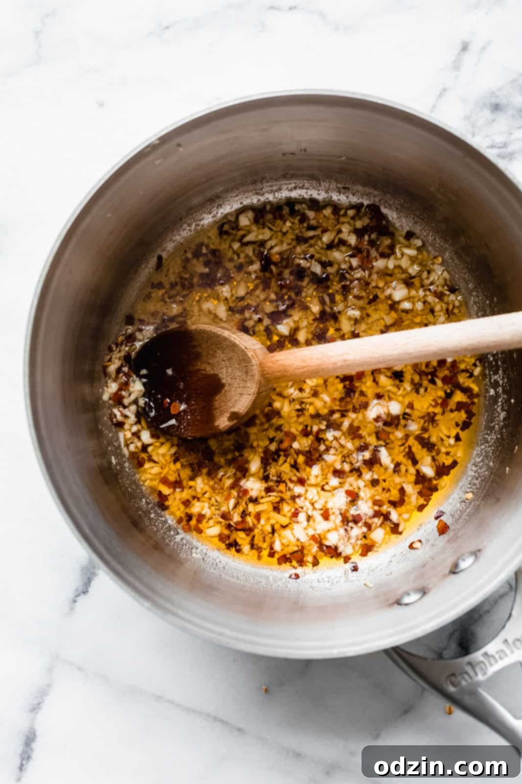 saucepan with olive oil, minced garlic, and red pepper flakes with wooden spoon resting inside