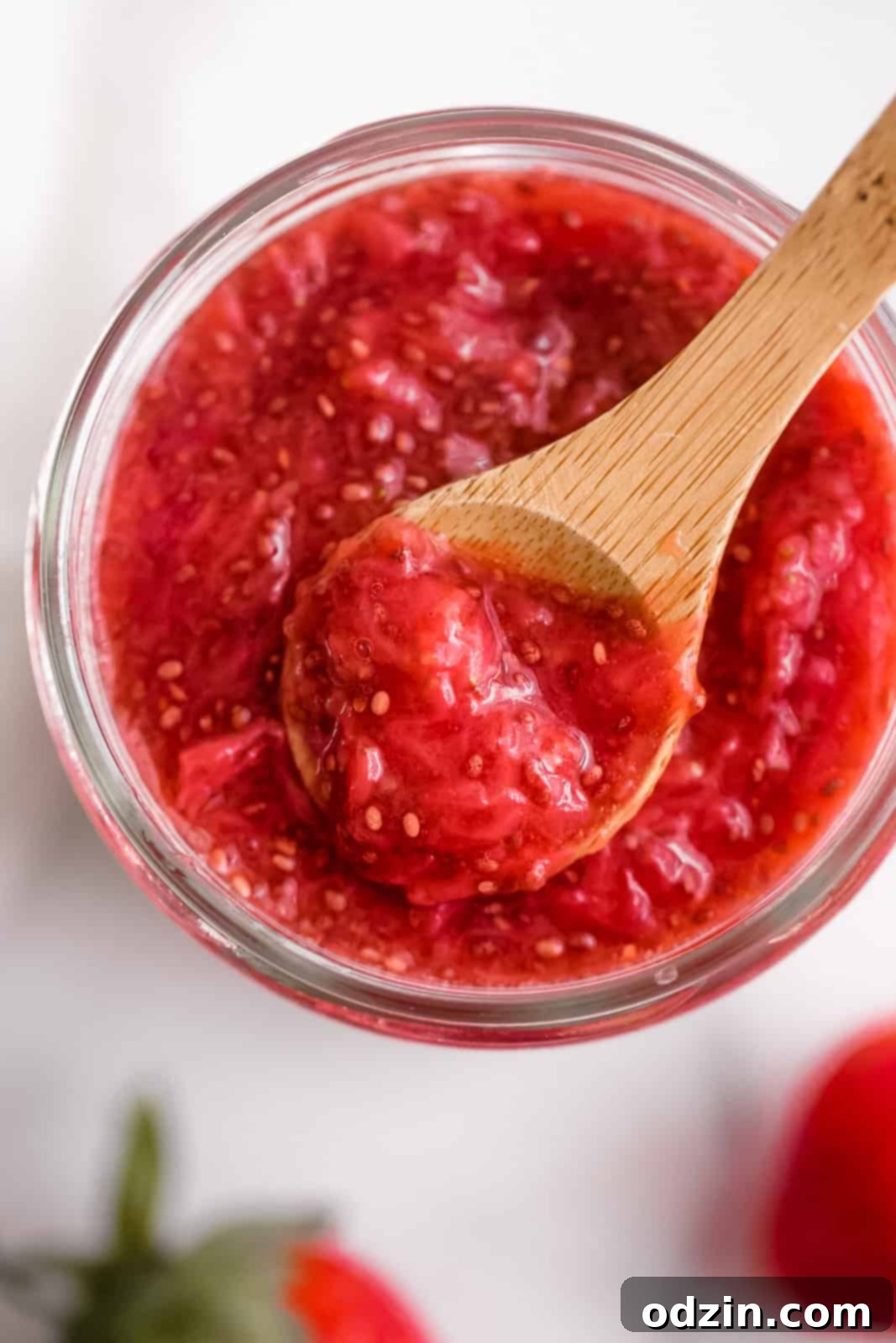 close up of glass jar with jam with a wooden spoon resting on top with jam