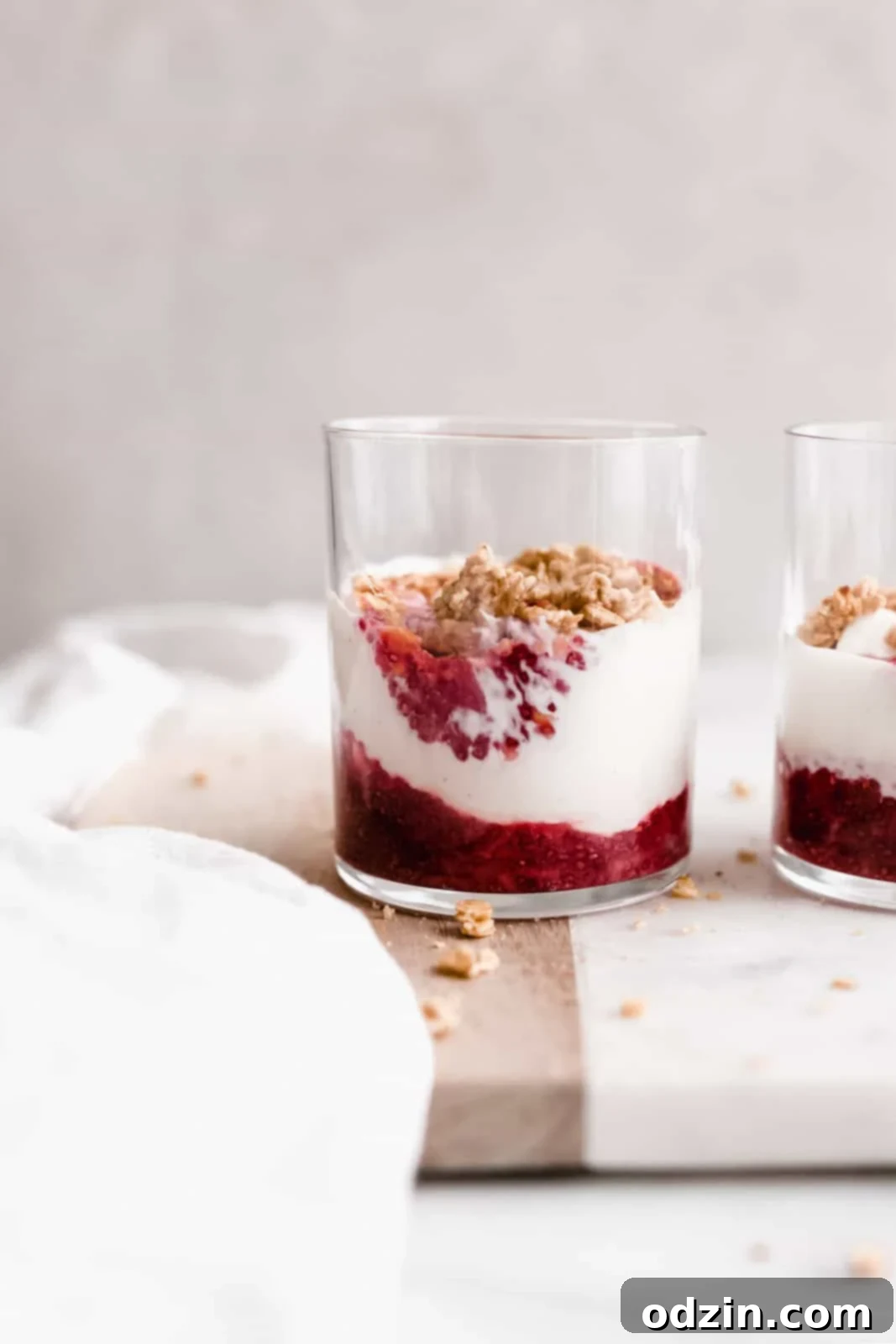 glass cups with jam and yogurt parfaits topped with granola on marble