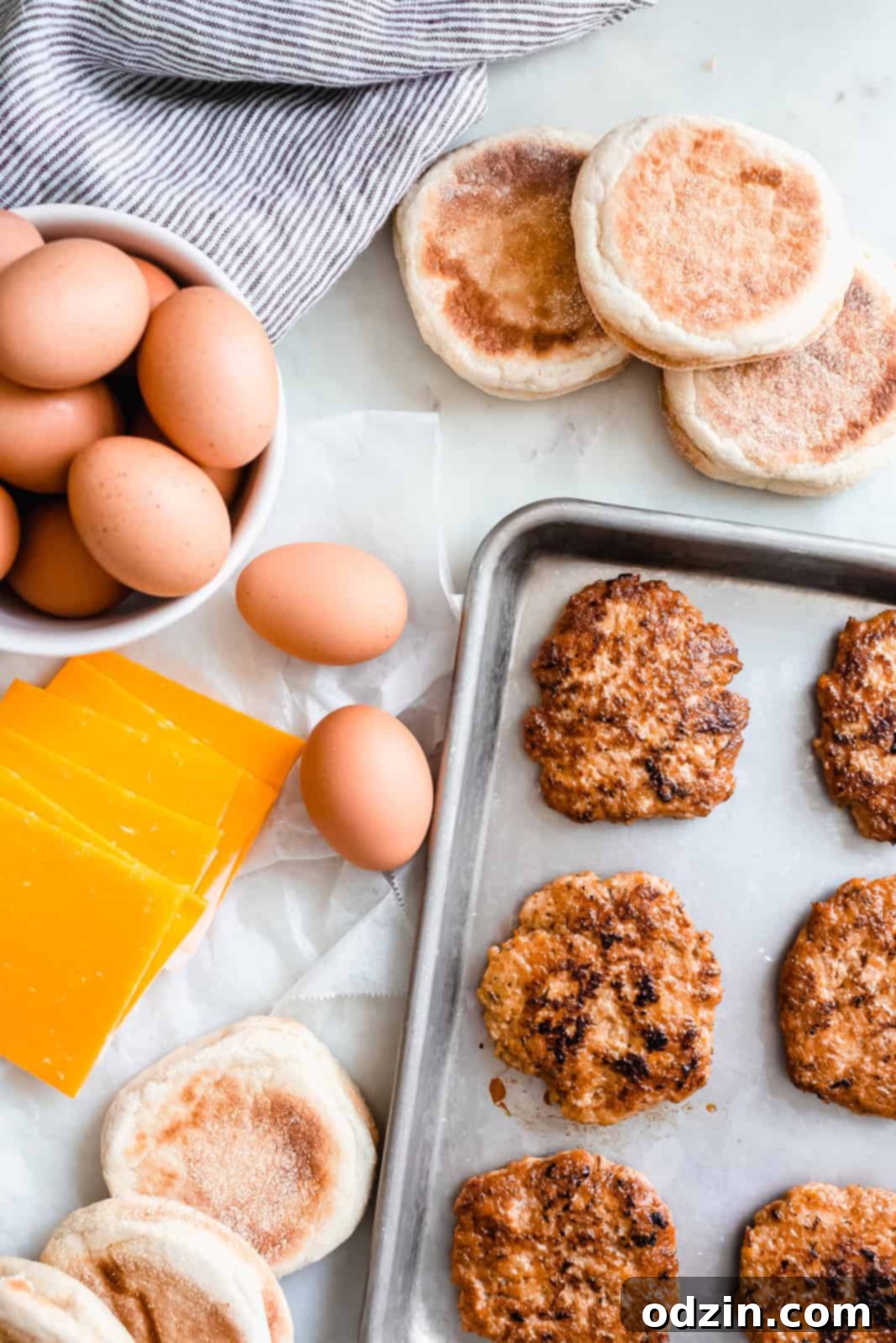 Ultimate Make-Ahead Chicken Sausage Egg and Cheese Sandwiches 4 All the fresh ingredients laid out on white marble for making freezer breakfast sandwiches, including chicken, eggs, English muffins, and cheese.