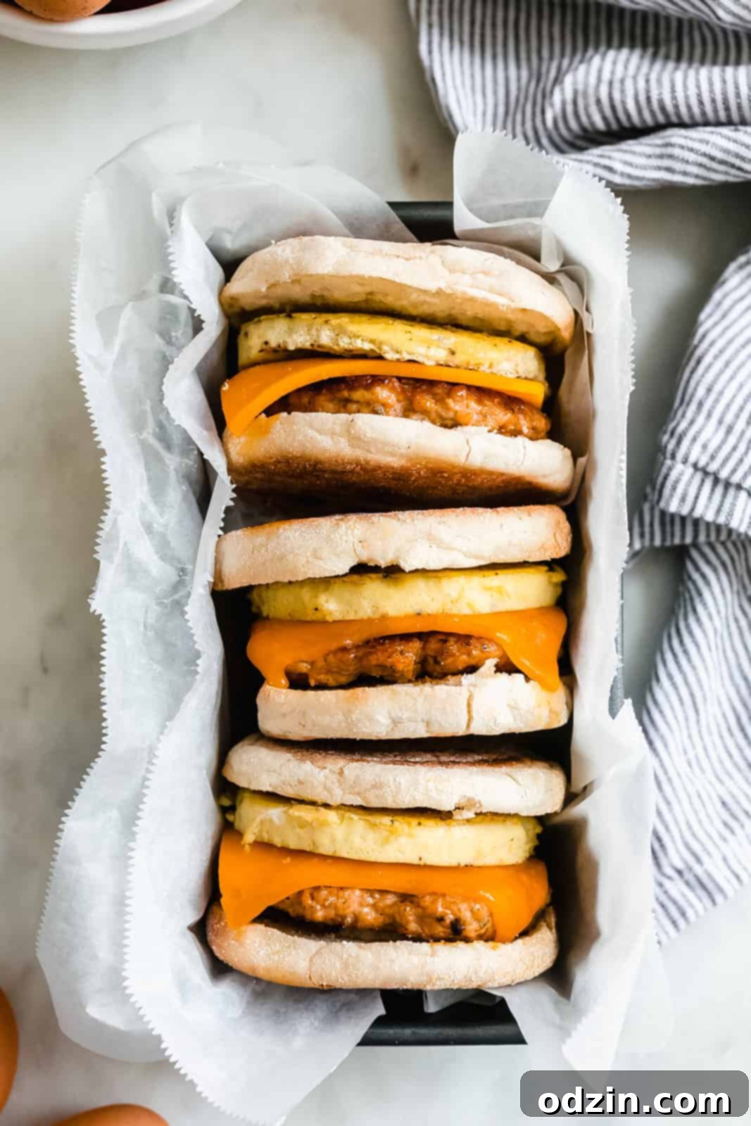Ultimate Make-Ahead Chicken Sausage Egg and Cheese Sandwiches 7 Three homemade breakfast sandwiches neatly arranged in a loaf pan lined with wax paper, ready for freezing.