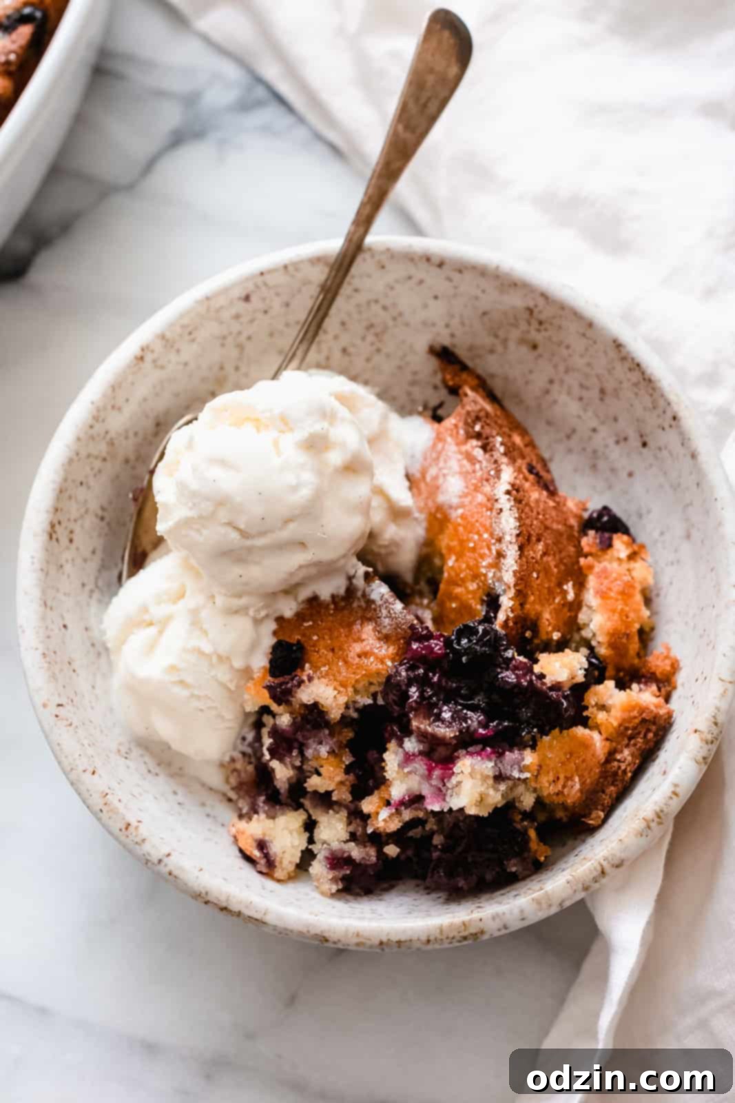 Effortless Texas Blueberry Cobbler 7 bowl with crumbled conbbler with melting vanilla ice cream and spoon