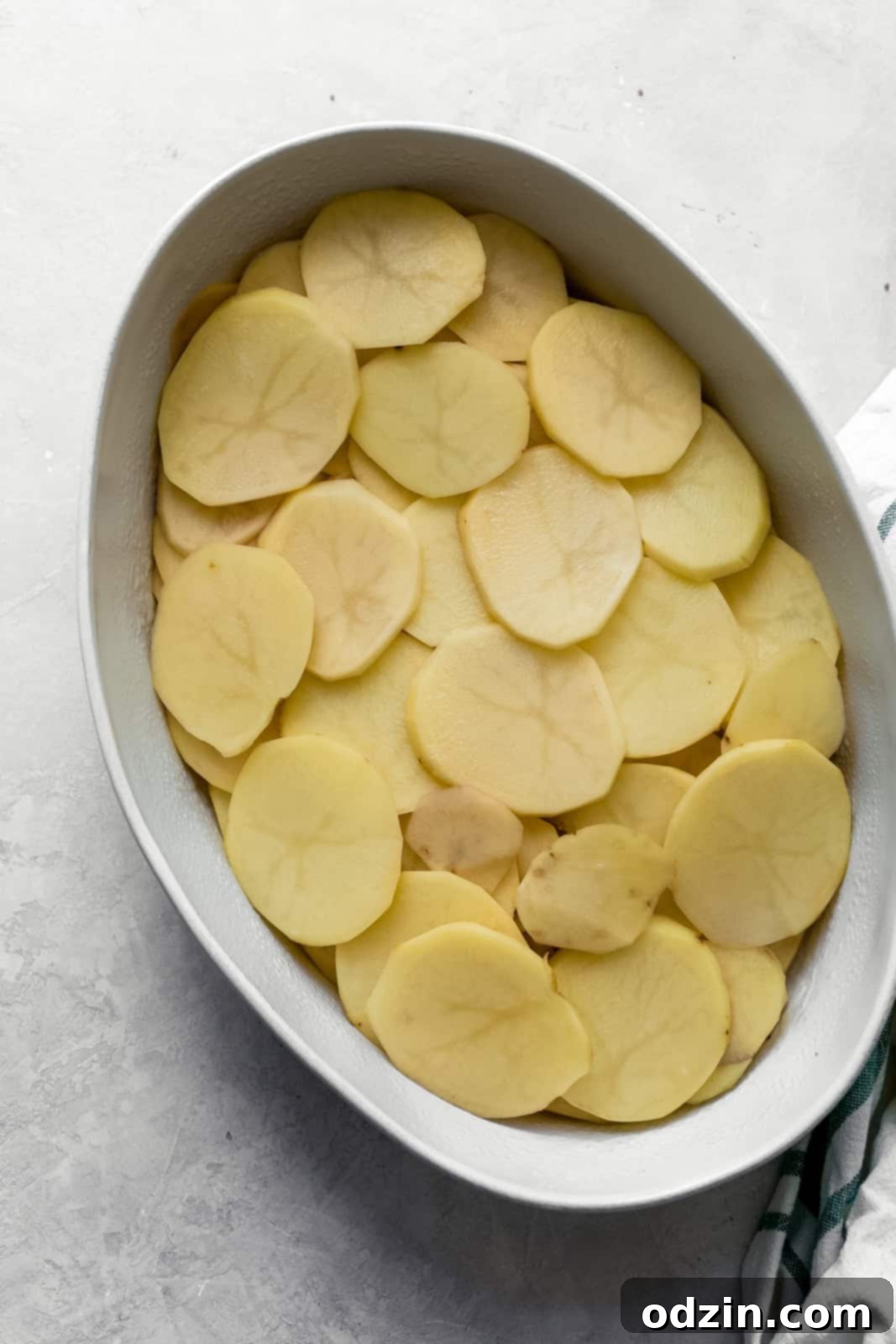 Creamy Cheesy Potato Gratin 4 thinly sliced potatoes in oval baking dish on gray surface