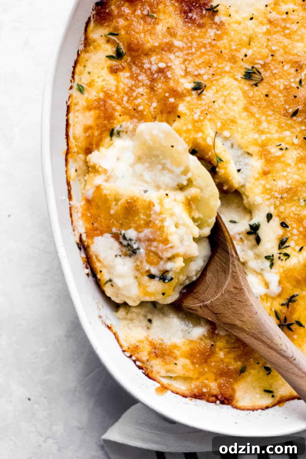Creamy Cheesy Potato Gratin 5 wooden spoon used to scoop sliced potatoes in cheese sauce topped with cheese