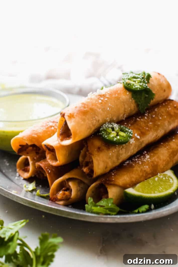 stacked chicken taquitos on platter with limes and sauce
