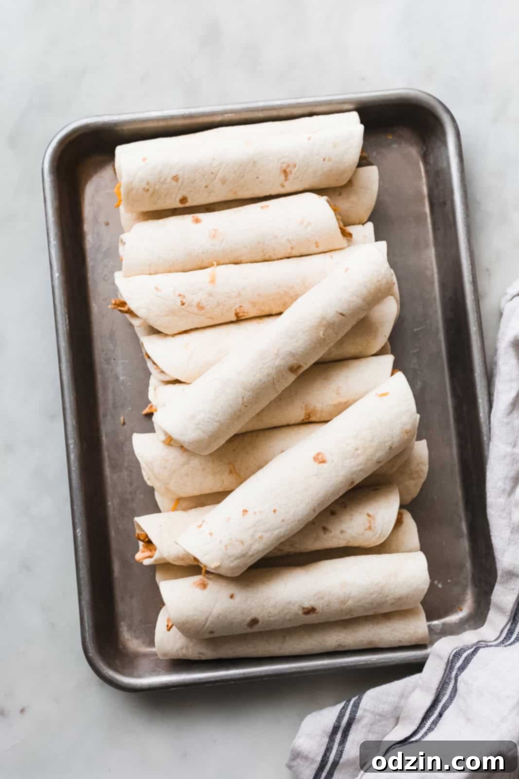 sheet pan with rolled chicken taquitos before frying