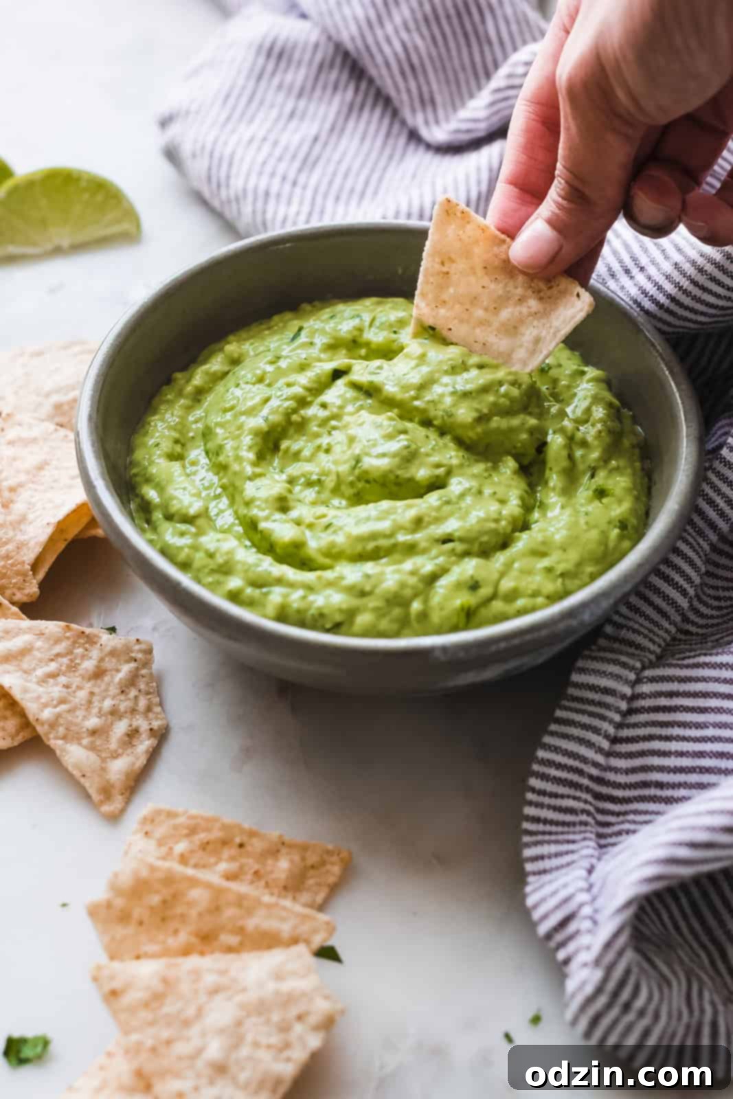 Velvety 5-Minute Avocado Dip 5 A bowl of creamy avocado dip with a hand dipping a tortilla chip into it, emphasizing its smooth and scoopable texture.