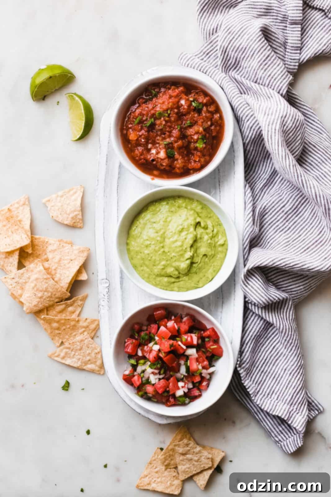 Velvety 5-Minute Avocado Dip 6 A beautiful food scene featuring an oval dish with three different types of delicious dips arranged on a white marble surface, inviting you to taste.