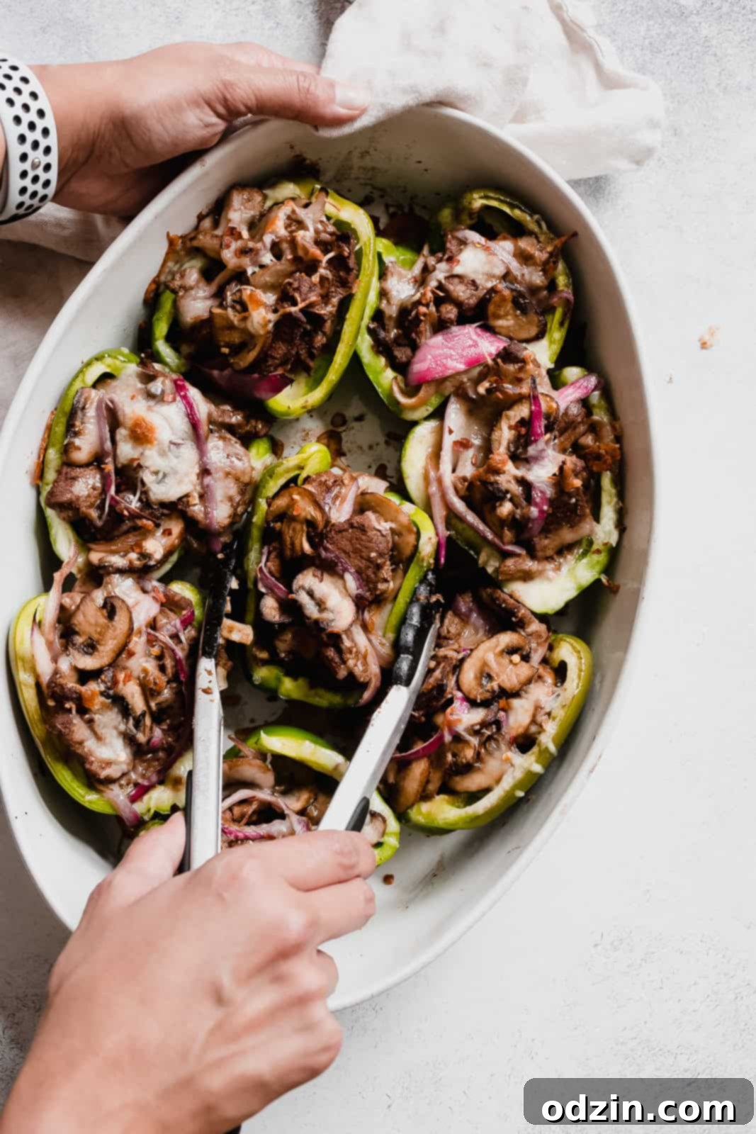 using tongs to grab stuffed peppers from oval dish