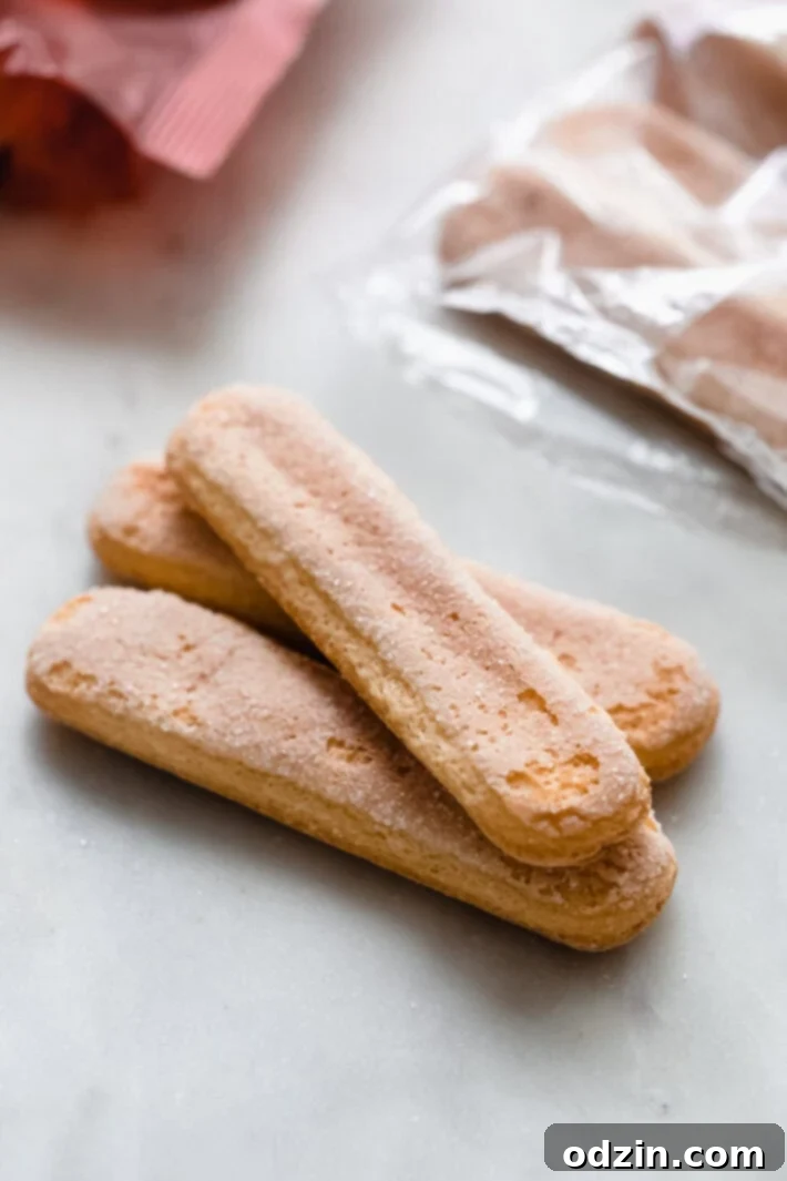 A pile of light, crisp ladyfingers (savoiardi biscuits) on a clean white marble surface, ready for dipping.