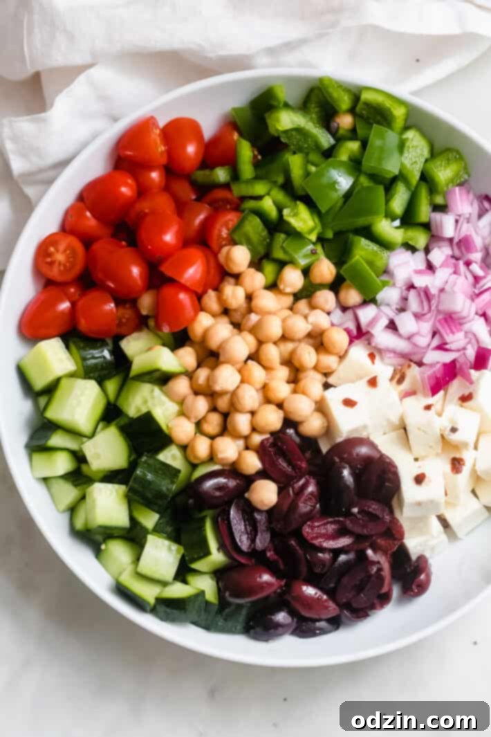 Marinated Feta Greek Salad - this is the best greek salad ever! It starts with feta that you marinated in olive oil with a few herbs and spices, then we'll toss it all together in a bowl with a homemade vinaigrette. Trust me, you'll never want a regular greeksalad again! #marinatedfeta #greeksalad #authenticgreeksalad #fetasalad #salad #saladrecipes | Littlespicejar.com ingredients for greek salad in a white bowl