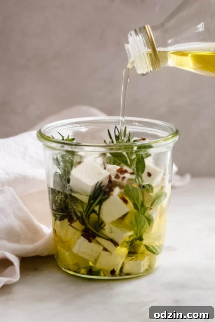 Hellenic Marinated Feta Salad 2 pouring oil into a glass jar with herbs and cubed feta cheese