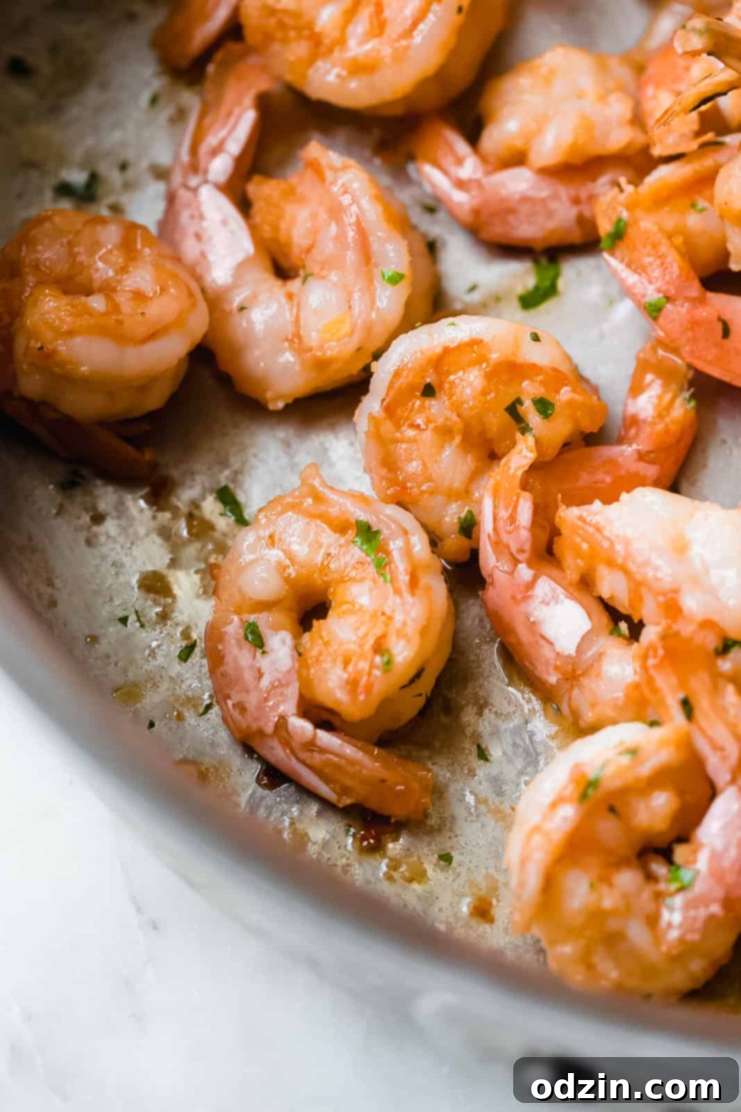 sautéed shrimp cooking in a stainless steel skillet, perfectly pink and curled