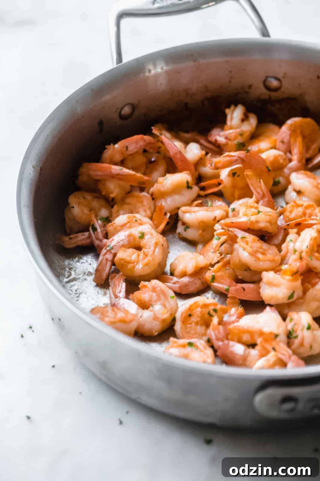 beautifully sautéed shrimp resting in a saute pan on a pristine white marble surface