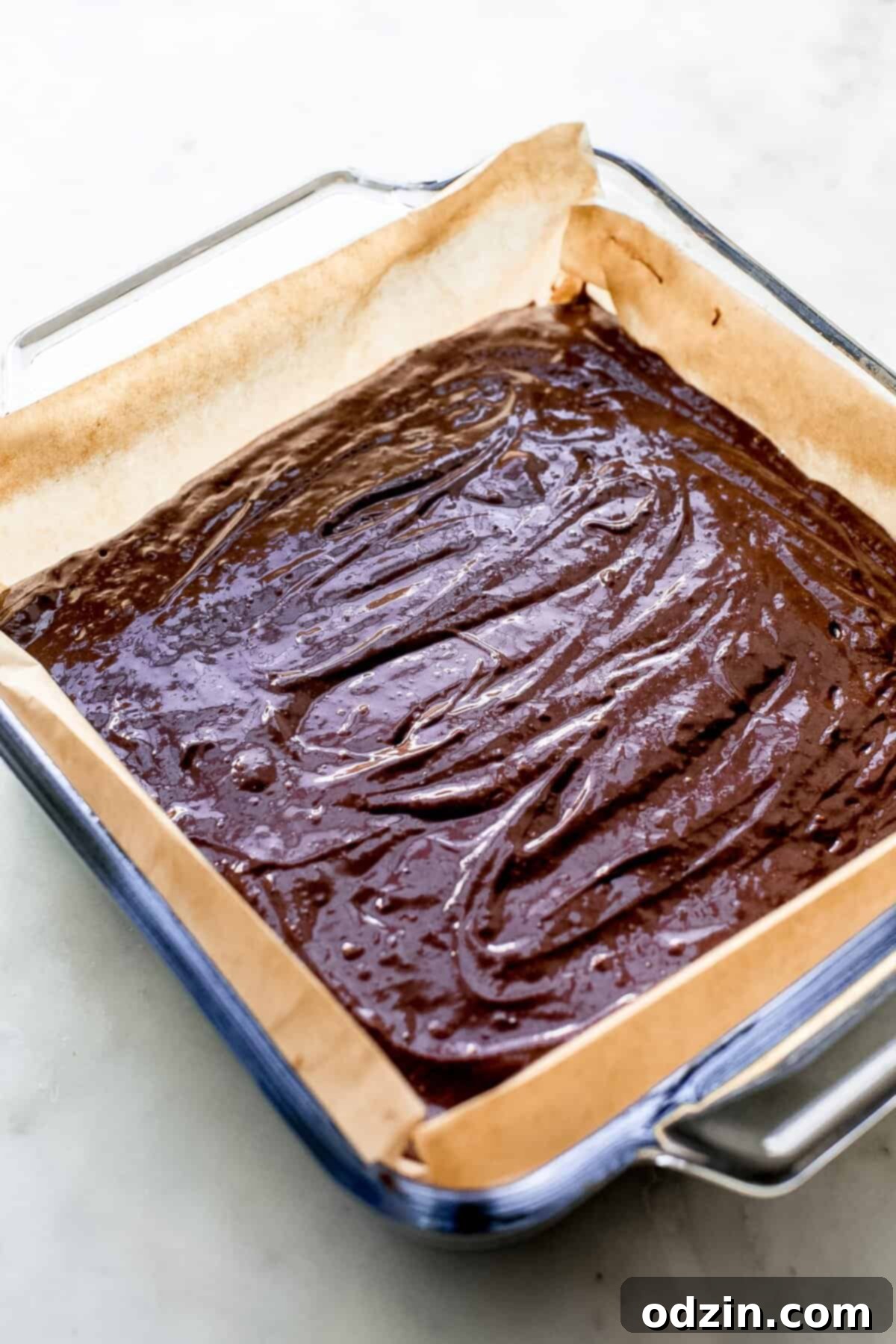 Decadent Pan-Banging Salted Fudge Brownies 7 fudge brownie mixture spread evenly in a glass baking dish lined with parchment paper