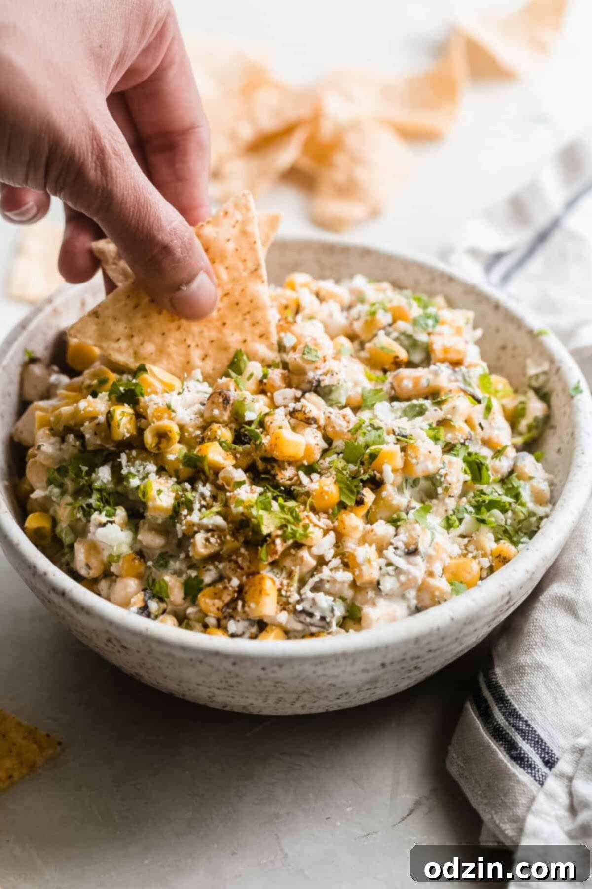 hand dipping corn tortillas in corn dip from bowl