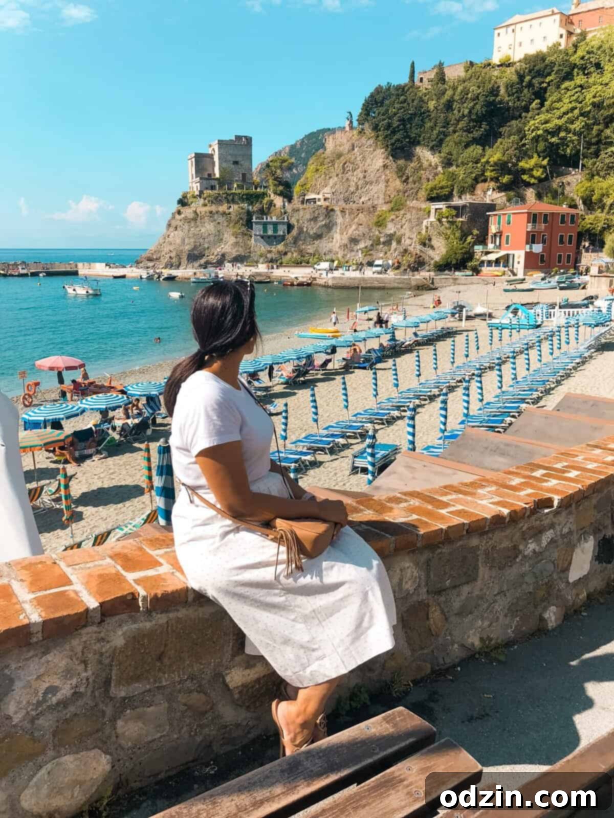 me sitting on a brick wall with the beach at Monterosso al Mar behind me
