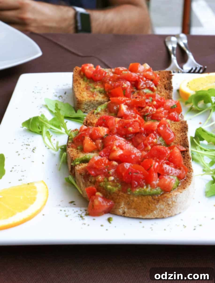 close up of toasted bread, topped with pesto and chopped tomatoes on a white plate